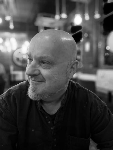 Barber 1 young man with beard smiling and wearing a brown shirt